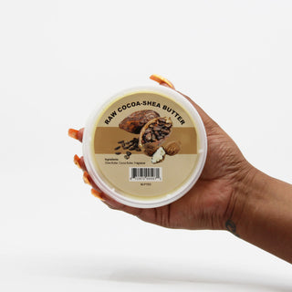 Hand holding a container of raw cocoa-shea butter with a visible label.