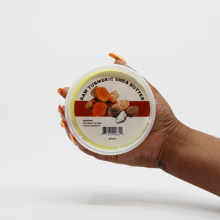 Hand holding a container of Raw Turmeric Shea Butter against a white background